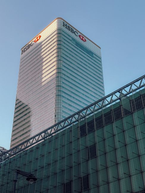 Close-up view of a modern commercial office building with a glass and metal facade, featuring numerous reflective windows arranged in a grid pattern. The building's exterior surface appears clean and